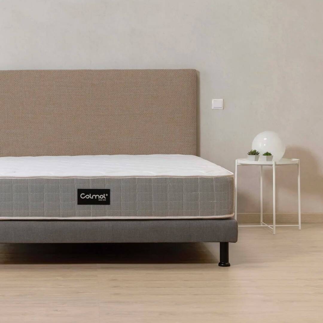 Colchão Colmol colocado sobre uma base de cama, com uma mesa de cabeceira ao lado. O chão é de madeira.